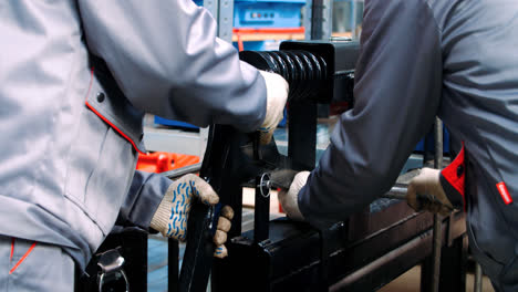 Workers-fixing-black-spring-shock-absorber-into-machine-for-processing