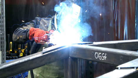 Welder-with-torch-and-protective-helmet-making-bright-sparks-during-welding