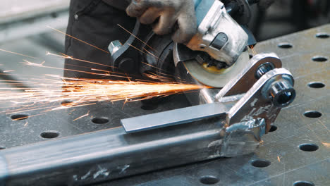 Worker-processing-surface-of-metal-part-with-angle-grinder-in-workshop