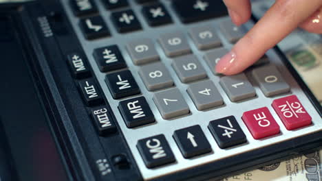 Business-woman-hand-using-calculator-at-office.-Calculator-on-dollar-banknotes