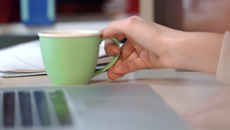 Business-woman-drink-coffee-in-office.-Woman-hand-holding-green-coffee-cup