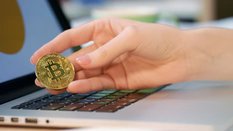 Woman-hand-holding-gold-bitcoin-coin-near-laptop-computer