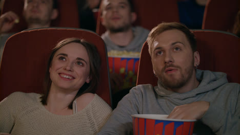 Young-couple-enjoying-film-in-cinema.-Couple-eating-popcorn-and-discussing-movie