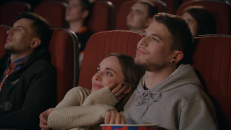Guy-embracing-girl-while-watching-movie-in-cinema.-Love-couple-enjoy-movie