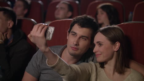 Girl-making-selfie-on-smartphone-with-boyfriend-in-movie-theatre