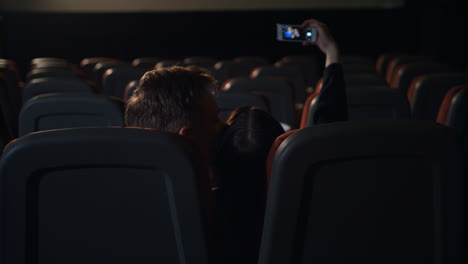 Young-people-kissing-in-empty-cinema-hall.-Love-couple-making-selfie-photo