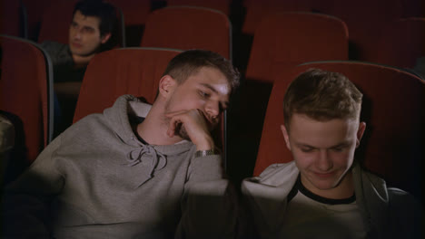 Two-guys-looking-smartphone-in-cinema.-Friends-having-fun-with-phone-at-theatre