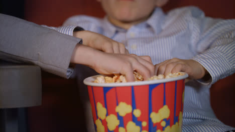 Children-hands-taking-popcorn-from-paper-box.-Cinema-food-for-kids