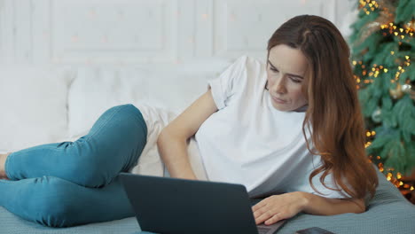 Concentrated-casual-woman-laying-with-laptop-computer-in-bedroom.