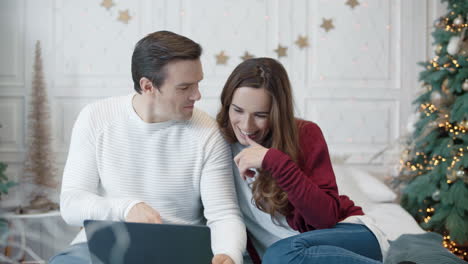 Relaxing-couple-looking-christmas-presents-on-pc-in-modern-apartment.
