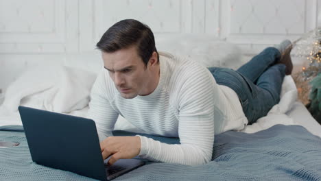 Concentrated-man-laying-with-computer-on-bed-in-luxury-house.
