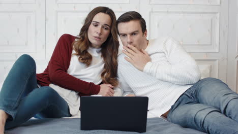 Sad-couple-watching-terrible-news-on-computer-at-home-together.