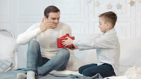 Surprised-father-getting-new-year-present-in-bedroom.-Happy-son-presenting-gift