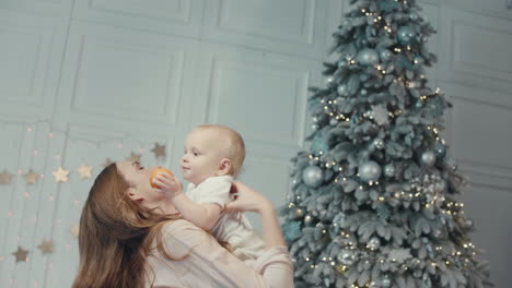 Cheerful-mother-kissing-cute-child-near-christmas-tree-in-modern-apartment.