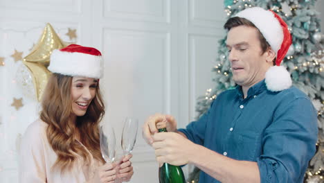 Lächelndes-Paar-Feiert-Neujahr-Mit-Champagner-In-Weihnachtsmützen.