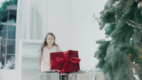 Glückliches-Mädchen,-Das-Eine-Geschenkbox-In-Der-Nähe-Des-Weihnachtsbaums-In-Einer-Modernen-Wohnung-Nimmt.