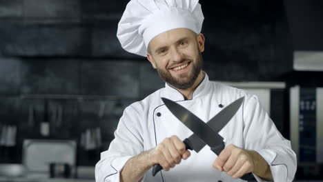 Mann-Koch-Hat-Spaß-Mit-Messern-In-Der-Küche.-Lächelnder-Koch,-Der-Gekreuzte-Messer-Schärft