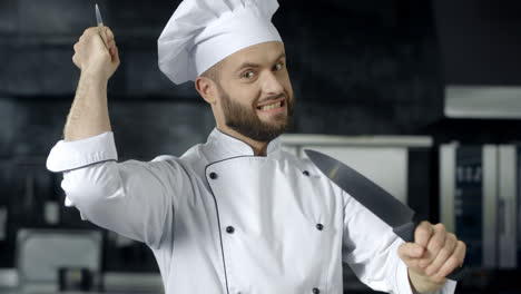 Chef-posing-with-knives-at-kitchen.-Chef-man-having-fun-with-tools-at-kitchen.