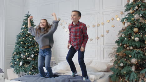 Two-smiling-teens-jumping-bed-in-luxury-house.-Cheerful-kids-having-jump-party