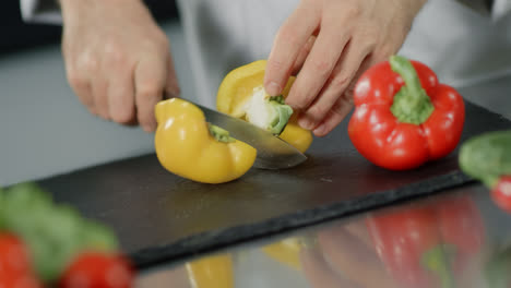 Chef-cooking-food-at-kitchen-restaurant.-Closeup-chef-hands-slice-yellow-pepper.