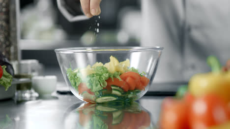 Chef-man-salting-salad-at-kitchen-restaurant.-Closeup-hand-salting-vegetables.