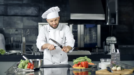 Male-chef-posing-at-professional-kitchen.-Cook-playing-with-sharpening-knives