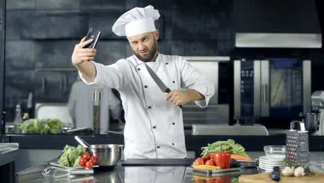 Chef-Haciendo-Fotos-En-La-Cocina.-Chef-Con-Cuchillo-Tomando-Selfie-En-El-Teléfono-Móvil.