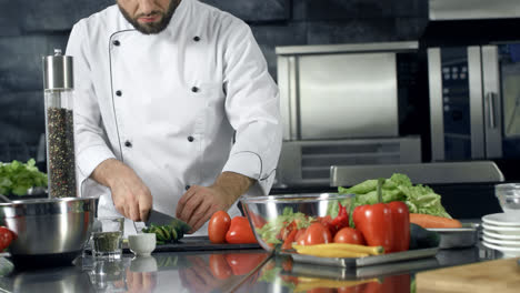 Chef-cooking-fresh-salad-at-kitchen.-Closeup-male-hands-cutting-cucumber.