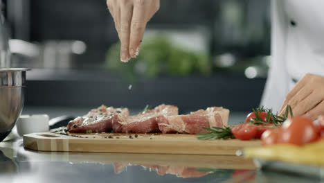 Male-chef-salting-meat-at-kitchen.-Closeup-chef-hands-salting-steak-at-workplace