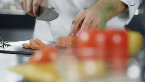 Chef-cutting-fish-at-professional-kitchen.-Closeup-chef-hands-slicing-salmon