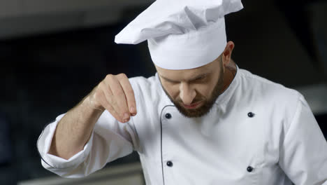Portrait-of-chef-cooking-at-professional-kitchen.-Serious-chef-salting-food.