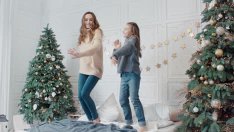 Happy-mother-and-daughter-jumping-up-and-down-on-bed-in-luxury-house.