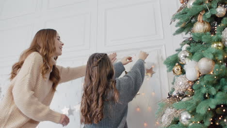 Smiling-mom-and-teen-daughter-putting-garland-on-wall-in-living-room.