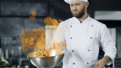 Man-chef-cooking-in-pan-with-fire-in-slow-motion-at-kitchen.-Young-chef