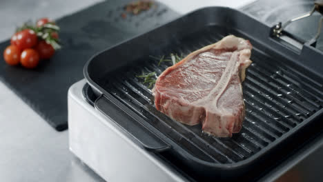 Fresh-steak-cooking-at-griddle-pan.-Closeup-raw-beef-grilling-at-cast-iron-pan