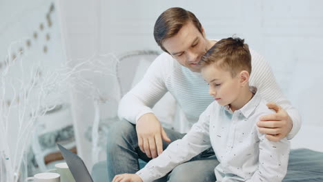 appy-father-hugging-son-looking-computer-screen-in-modern-apartment.