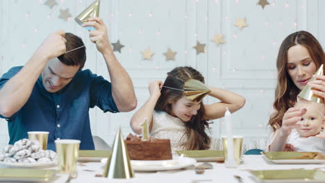 Funny-family-putting-party-hat-in-luxury-house.-Happy-couple-with-two-kids