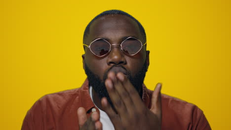 Portrait-of-handsome-afro-man-sending-air-kiss-to-camera-on-yellow-background.