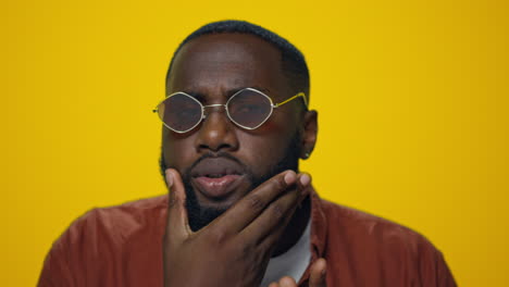 Portrait-of-serious-african-american-man-checking-beard-on-yellow-background.