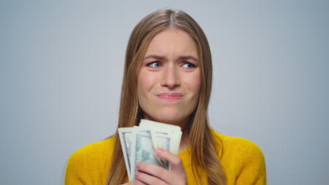Portrait-of-upset-woman-counting-money-on-grey-background-in-studio.