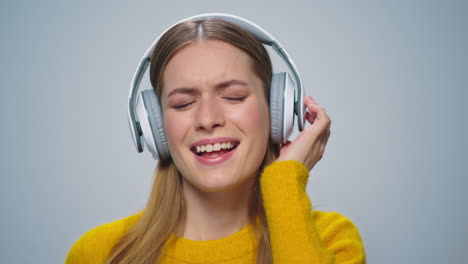 Primer-Plano-Mujer-Sonriente-Escuchando-Música-En-Auriculares-Sobre-Fondo-Gris.
