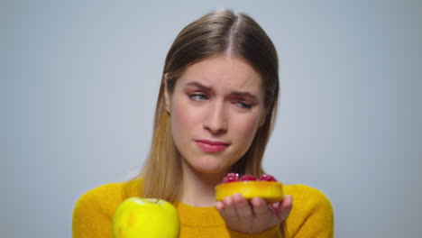 Portrait-of-thoughtful-woman-selecting-between-apple-or-cake-at-camera.