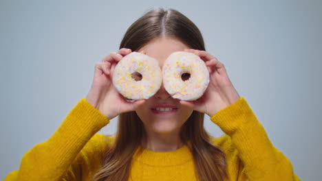 Portrait-of-smiling-woman-having-fun-with-donuts-at-camera-on-grey-background.