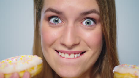 Closeup-joyful-woman-eating-donut-with-big-appetite-on-grey-background.