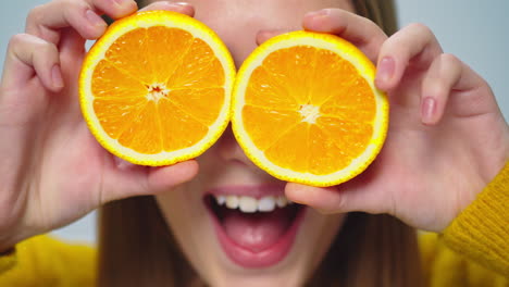 Closeup-young-pretty-woman-making-faces-with-two-orange-slices-indoors.