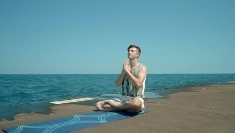 Man-sitting-by-sea-in-lotus-position-then-standing-on-his-head.-Man-doing-yoga