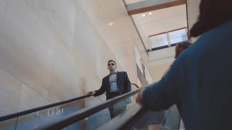 Modern-man-in-stylish-suit-and-sunglasses-going-down-on-escalator