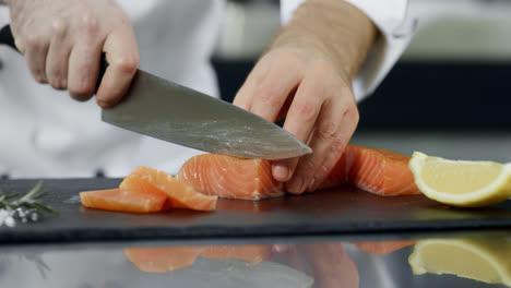 Chef-cutting-salmon-fillet-at-kitchen.-Closeup-hands-slicing-fresh-fish.