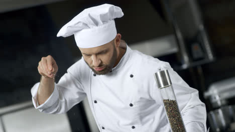 Portrait-of-man-chef-salting-food-at-kitchen.-Concentrated-chef-cooking-meal
