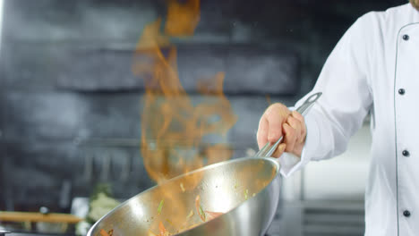 Chef-cooking-food-with-fire-flame-in-pan-at-kitchen.-Chef-hands-preparing-food